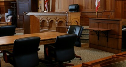 Empty courtroom with wooden desks and chairs, judge's bench at the front, American flag, and ornate wood paneling—a setting familiar to Chicago lawyers specializing in intellectual property law.