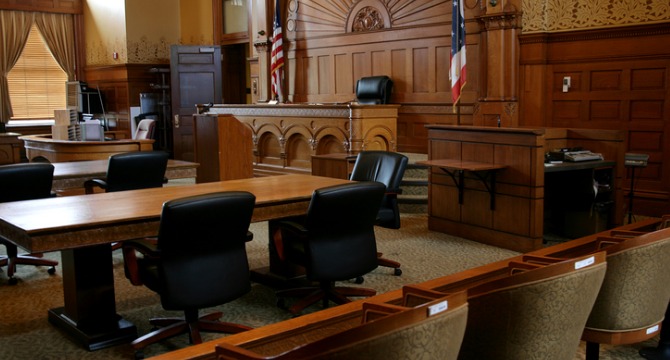 Empty courtroom with wooden furnishings, judge's bench, jury box, witness stand, and American flag visible; no people present—an atmosphere familiar to Chicago lawyers and law offices handling important cases.