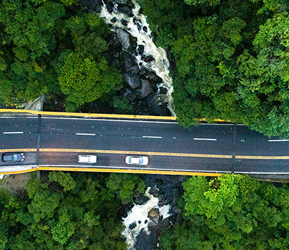 Aerial view of a curved road with three cars driving through dense green forest over a small river—an inspiring scene for lawyers in Chicago seeking tranquility outside the city.