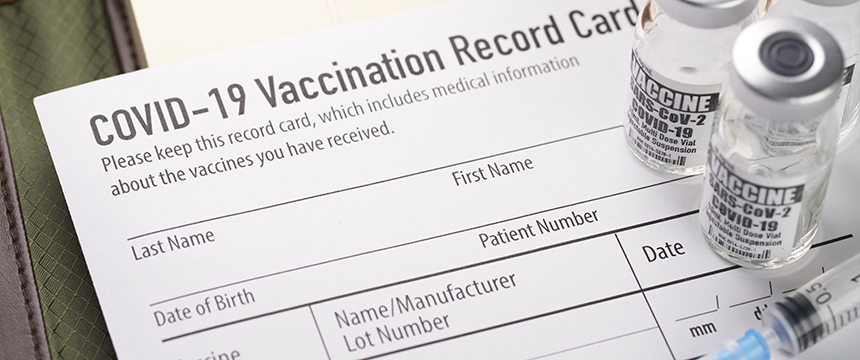 A COVID-19 vaccination record card lies on a table next to three vaccine vials and a syringe, a scene not uncommon in corporate law offices as chicago lawyers prioritize health and safety.