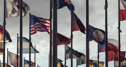 Multiple national flags from different countries are displayed on flagpoles against a cloudy sky, reflecting the international reach of a corporate law office or lawyers in Chicago specializing in global litigation support.