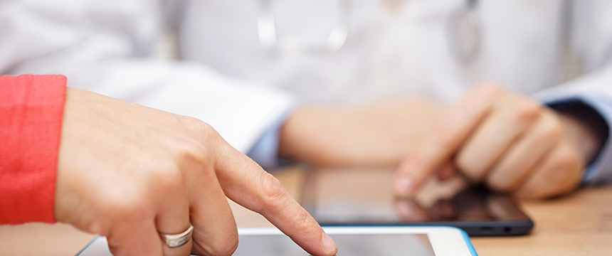 Two people use touchscreens on electronic devices, with one person's hand in the foreground and another, possibly from law offices or litigation support, wearing a white coat in the background.