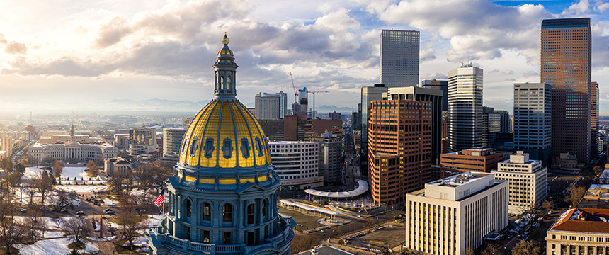 Aerial view of a city skyline with the gold-domed capitol building in the foreground, tall office buildings housing leading law offices and Chicago lawyers in the background, all under a partly cloudy sky.