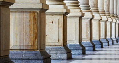 A row of stone columns with square bases and fluted shafts stands along a marble floor in an architectural colonnade, evoking the timeless elegance found in prestigious Chicago law offices.