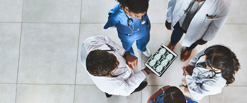 Five medical professionals stand in a circle, looking at brain scans displayed on a tablet held by one of them, discussing concerns about intellectual property law and how it might impact their groundbreaking research.