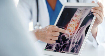 A doctor points to a spinal X-ray displayed on a tablet while discussing it with a patient, providing insights that can assist chicago lawyers with litigation support.