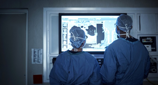 Two surgeons in scrubs and caps examine medical scans displayed on a large monitor in an operating room, similar to how law offices review critical evidence for litigation support.