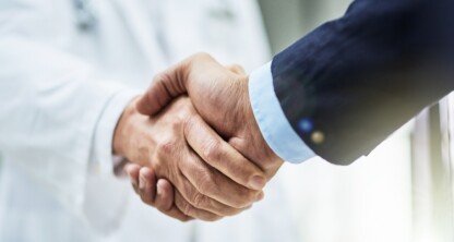 A doctor in a white coat and stethoscope shakes hands with a person in a suit, illustrating a professional partnership between healthcare experts and chicago lawyers for litigation support.