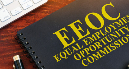 A notebook with "EEOC Equal Employment Opportunity Commission" written in yellow beside a pen and part of a computer keyboard on a wooden desk, perfect for law offices or lawyers in Chicago handling employment matters.