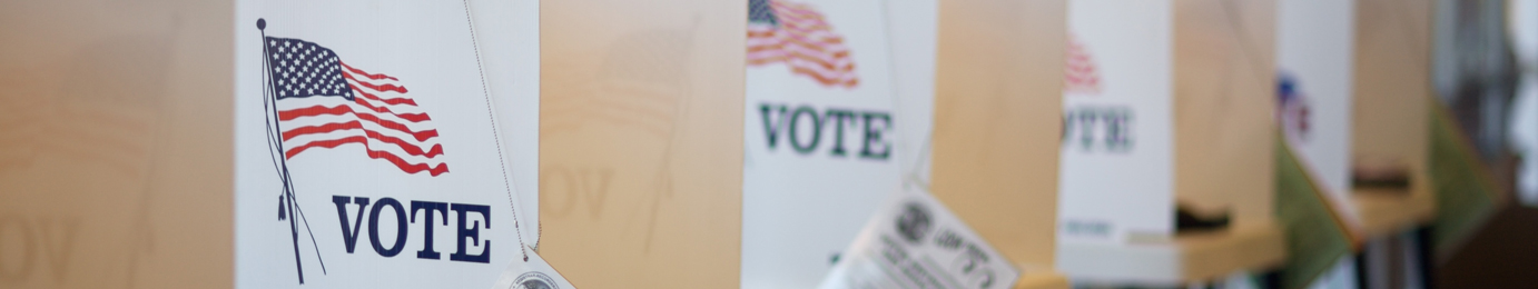 Row of voting booths with American flags and the word "VOTE" displayed, set up indoors for an election, similar to dedicated spaces used by lawyers in Chicago for confidential consultations or litigation support.