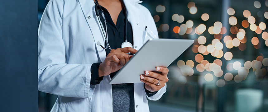 A doctor in a white coat uses a tablet, with a stethoscope around their neck and blurred lights in the background, reflecting the modern professionalism often found in Chicago lawyers and law offices.