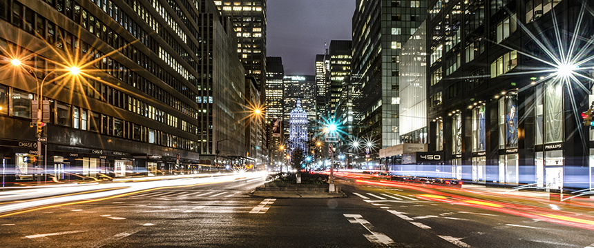A busy city street at night with tall buildings, bright lights, and blurred car headlights—home to top law offices and lawyers in Chicago working late into the evening.