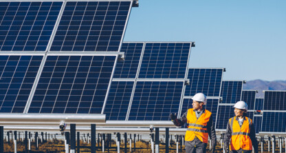 Two workers in safety vests and helmets walk near rows of solar panels at a solar farm, a symbol of sustainability that even Chicago lawyers at a corporate law office might applaud on a clear day.