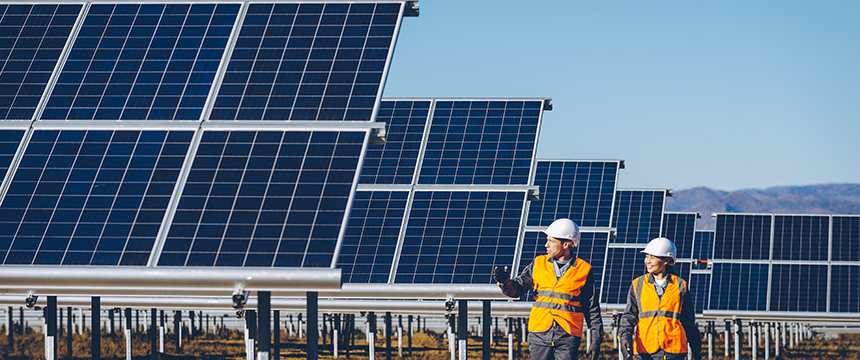Two workers in safety vests and helmets walk near rows of solar panels at a solar farm, a symbol of sustainability that even Chicago lawyers at a corporate law office might applaud on a clear day.