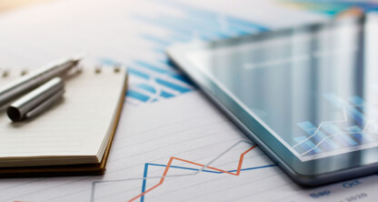 A tablet, pen, and notepad rest on papers displaying financial charts and graphs, essential tools for law offices and litigation support.