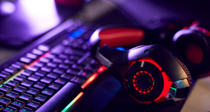A pair of black and red gaming headphones rests on a backlit mechanical keyboard with multicolored RGB lighting in a Chicago corporate law office.