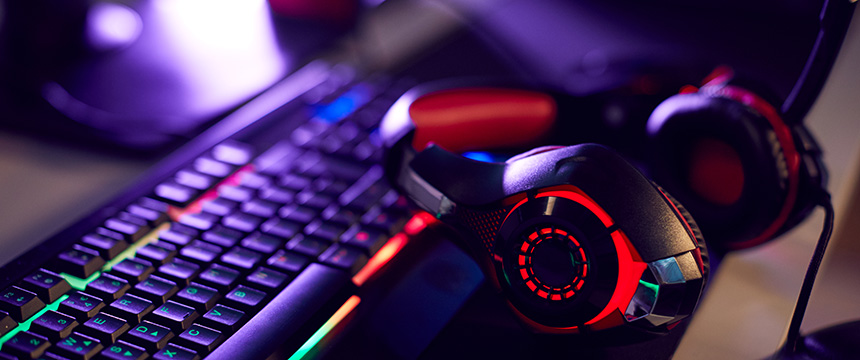 A pair of black and red gaming headphones rests on a backlit mechanical keyboard with multicolored RGB lighting in a Chicago corporate law office.