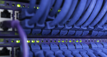 Close-up view of network switches with blue Ethernet cables plugged in and status lights illuminated, ensuring secure connectivity for a corporate law office’s litigation support and intellectual property law operations.
