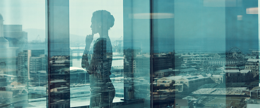 A woman stands in front of a window in a high-rise building, looking out over a cityscape with buildings and a ferris wheel visible in the distance—an inspiring view for lawyers in Chicago handling complex cases.