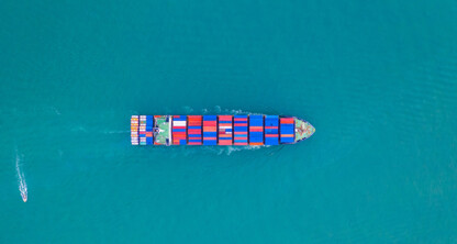 Aerial view of a large cargo ship with colorful containers sailing in open blue water, with a small boat nearby—ideal imagery for law offices or lawyers in Chicago specializing in maritime and intellectual property law.