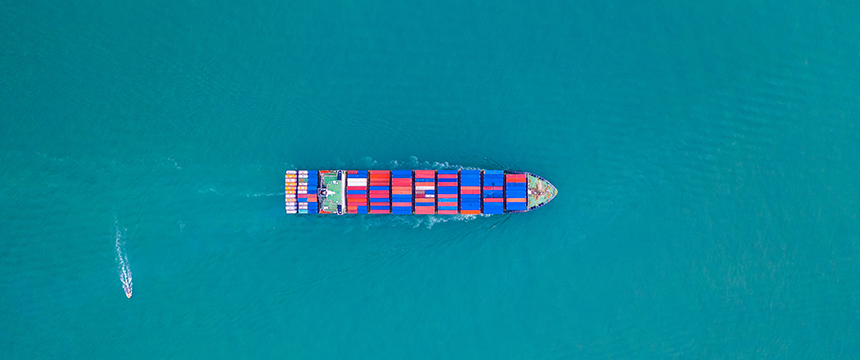 Aerial view of a large cargo ship with colorful containers sailing in open blue water, with a small boat nearby—ideal imagery for law offices or lawyers in Chicago specializing in maritime and intellectual property law.