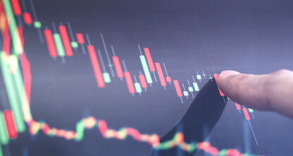 A hand points at a digital screen displaying a candlestick chart with fluctuating red and green lines, representing financial market data—ideal for use by law offices offering litigation support in financial cases.