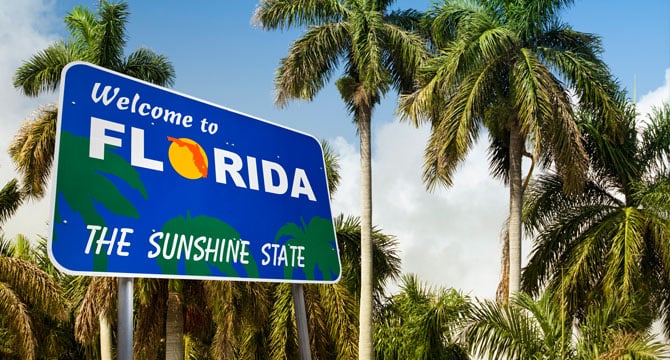 A blue "Welcome to Florida, The Sunshine State" sign with palm trees in the background under a partly cloudy sky—far from the skyline of Chicago lawyers or a bustling corporate law office.