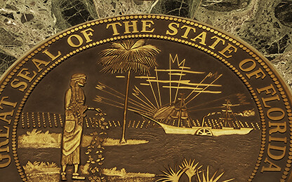 Bronze Great Seal of the State of Florida embedded in a green marble surface, surrounded by rope barriers and two smaller bronze medallions—a distinguished display often seen in prestigious law offices.