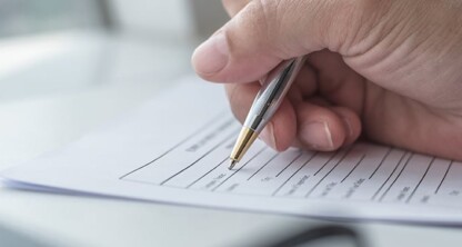 A hand holding a pen fills out a form with printed lines and text on a stack of papers, typical of tasks handled in corporate law offices or by lawyers in Chicago.