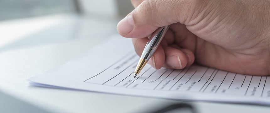 A hand holding a pen fills out a form with printed lines and text on a stack of papers, typical of tasks handled in corporate law offices or by lawyers in Chicago.