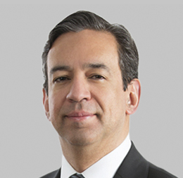 A man with short dark hair wearing a black suit, white shirt, and tie is posed against a plain light gray background, reflecting the professionalism found in top Chicago lawyers and law offices.