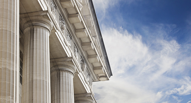 Close-up view of classical building columns and ornate architectural details against a partly cloudy blue sky, evoking the prestige and tradition often associated with Chicago lawyers.