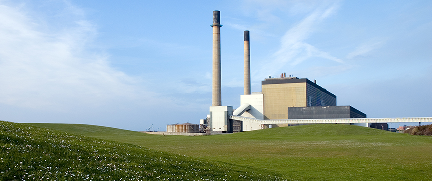 A power plant with two tall smokestacks stands behind a grassy field under a partly cloudy sky, much like law offices providing diligent litigation support amid the landscape of intellectual property law.