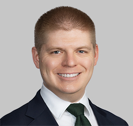 Man in a suit and tie smiling at the camera with a neutral gray background, representing the professionalism you can expect from top chicago lawyers.