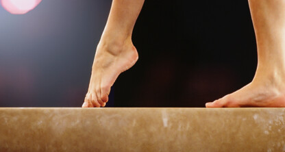 Close-up of a person's bare feet balancing on a gymnastics balance beam, with a dark blurred background—symbolizing the precision and balance required in litigation support for law offices.