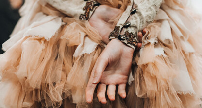 Close-up of a person’s hands clasped behind their back, wearing a ruffled, peach-colored tulle dress with ornate sleeve details—an elegant look that stands out at events hosted by intellectual property law firms in Chicago.