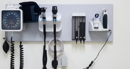 Wall-mounted medical equipment including a blood pressure monitor, otoscope, ophthalmoscope, thermometer, and containers for disposable covers in a clinical setting often found in Chicago lawyers’ offices offering on-site health services.