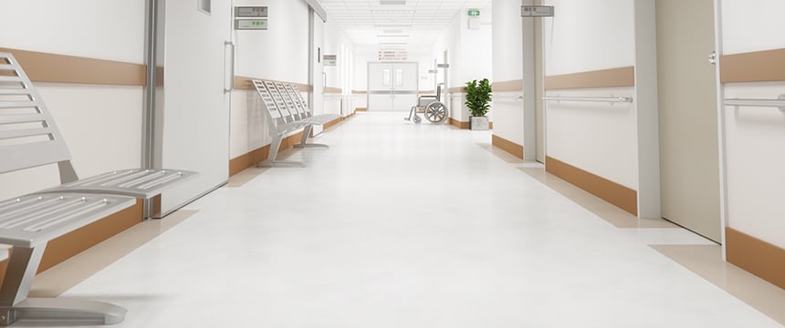 Empty hospital corridor with metal benches, beige and white walls, handrails, a wheelchair near the end, and doors on either side—an atmosphere as quiet as law offices specializing in intellectual property law.