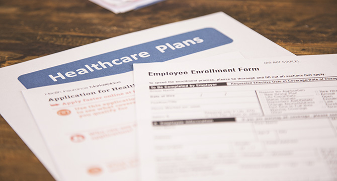 Two documents on a desk: one titled "Healthcare Plans" and another labeled "Employee Enrollment Form," both related to health insurance at a Chicago law office.