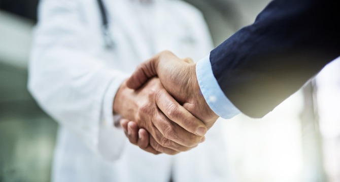 A doctor and a lawyer in Chicago are shaking hands, with the focus on their handshake and the doctor wearing a white coat.