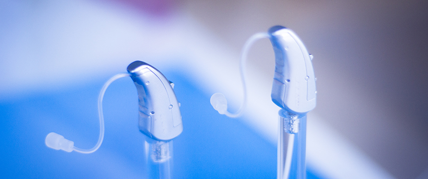 Two silver hearing aids are displayed upright on clear stands against a blurred blue and purple background, reminiscent of the professionalism seen in top Chicago lawyers' offices.