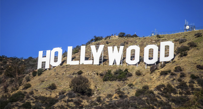 The Hollywood sign stands on a hillside against a clear blue sky, with sparse vegetation and a fence visible nearby—far from the bustling offices of chicago lawyers.