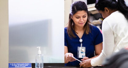 A woman in blue scrubs assists another person at a reception desk, handing over a card. A bottle of hand sanitizer is on the counter, highlighting the attention to detail often valued by lawyers in Chicago seeking reliable litigation support.