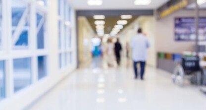 Blurred view of a hospital corridor with people walking, a wheelchair near a counter, and bright lighting from overhead fixtures—much like the busy atmosphere found in law offices or among Chicago lawyers offering litigation support.