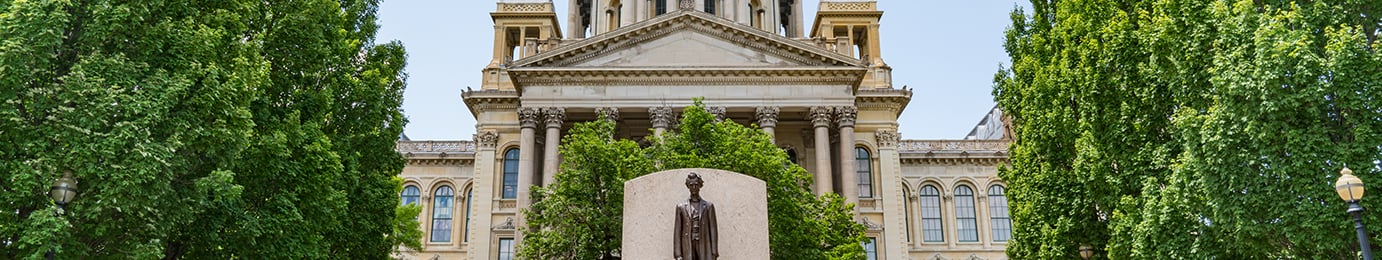A statue of a man stands in front of a historic government building, surrounded by tall green trees—a fitting scene for lawyers in Chicago specializing in intellectual property law.
