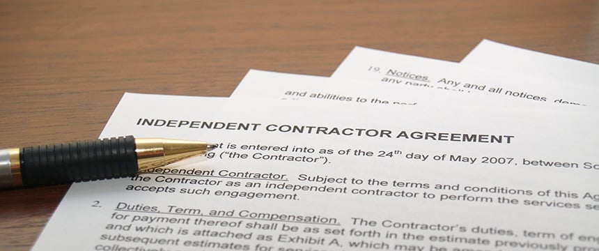 A pen rests on a stack of papers titled "Independent Contractor Agreement," placed on a wooden surface in a corporate law office led by experienced Chicago lawyers.