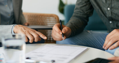 Two people sit at a table discussing documents, with one person holding a pen above a paper and the other pointing at the document—a typical scene at law offices handling intellectual property law matters.