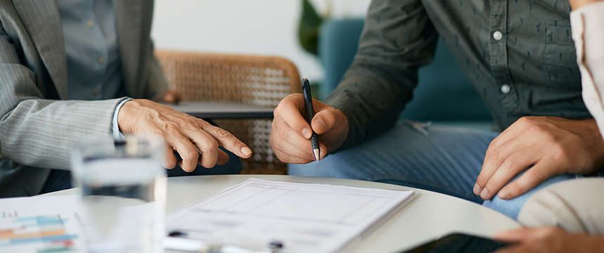 Two people sit at a table discussing documents, with one person holding a pen above a paper and the other pointing at the document—a typical scene at law offices handling intellectual property law matters.