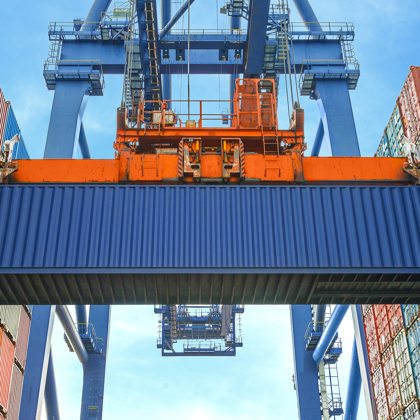 A large blue crane is lifting a blue shipping container at a port, where stacked containers line either side—an impressive scene that's often referenced in discussions of corporate law office logistics and international trade.