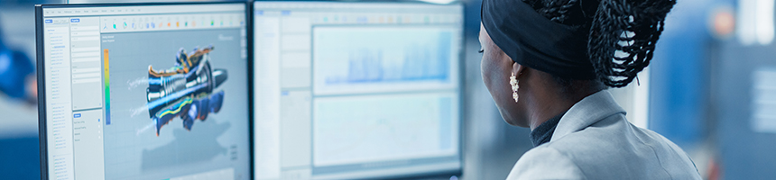 A woman sits at a desk in a law office, working on two monitors displaying technical graphics and charts—providing essential litigation support for intellectual property law cases.